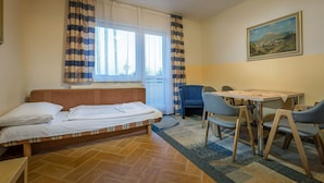 A room with a bed, a dining table with chairs, a window with curtains, and a painting on the wall. - Miramonti Apartmany (Vysoké Tatry)