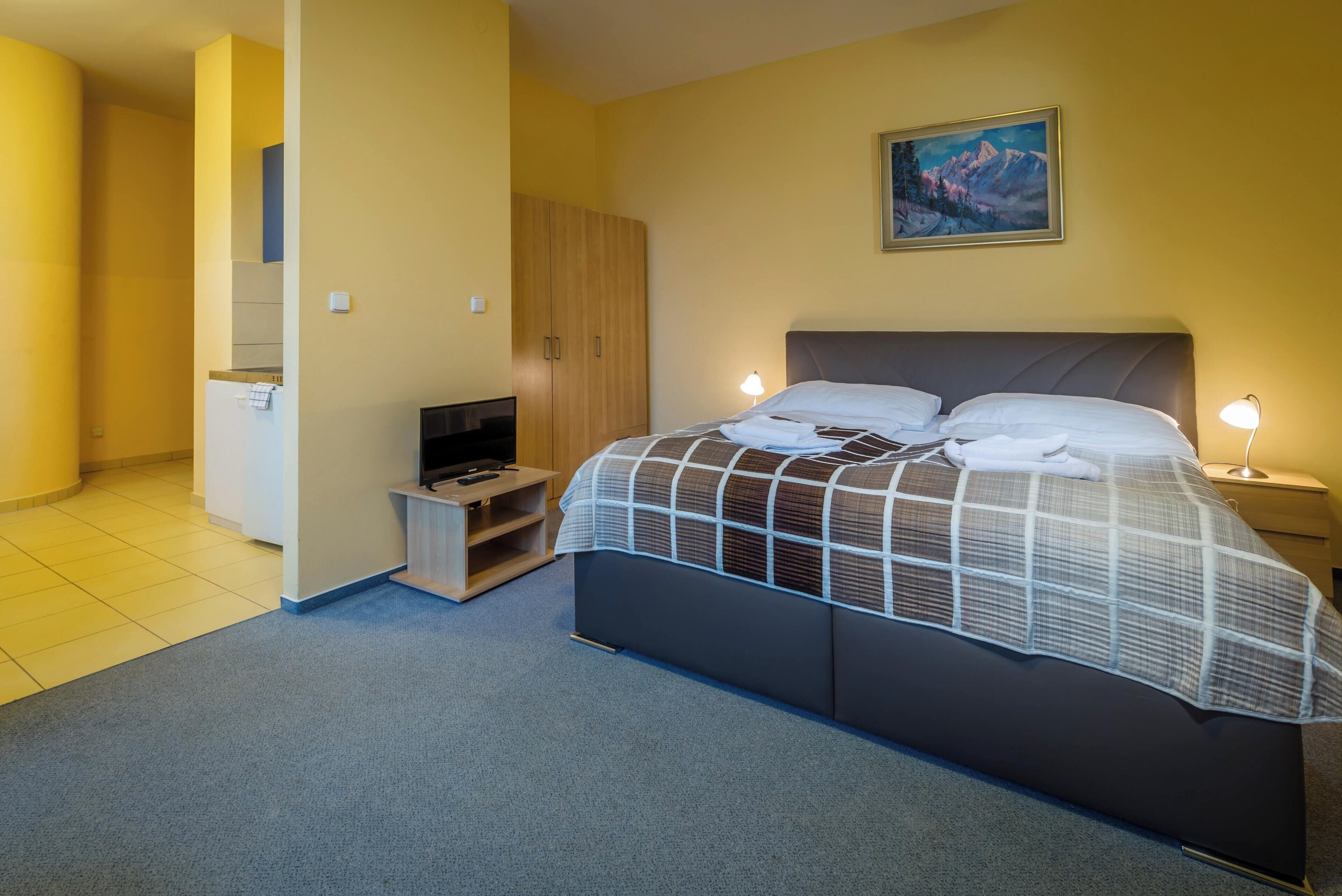 A bedroom with a bed, bedside lamps, a TV, a wardrobe, and a painting on the wall.