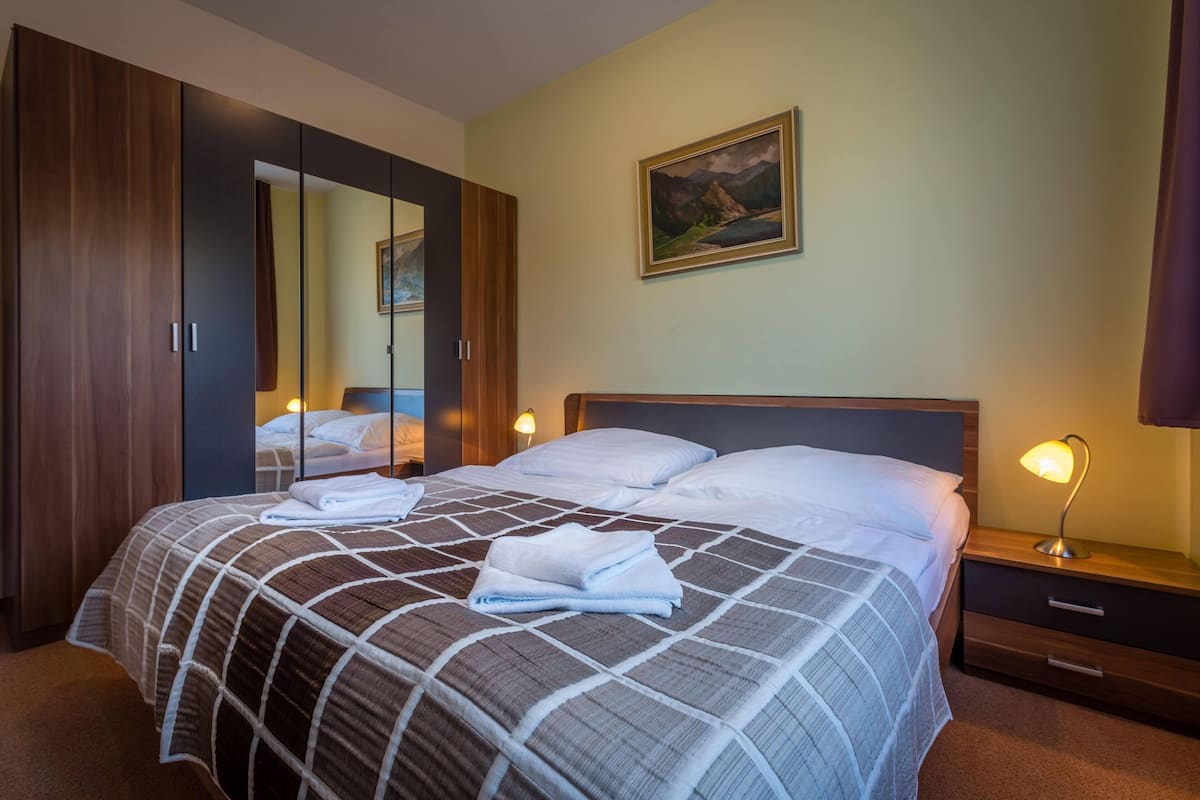 Una habitación de hotel con una cama grande, un armario, una mesita de noche con lámpara y un cuadro en la pared.