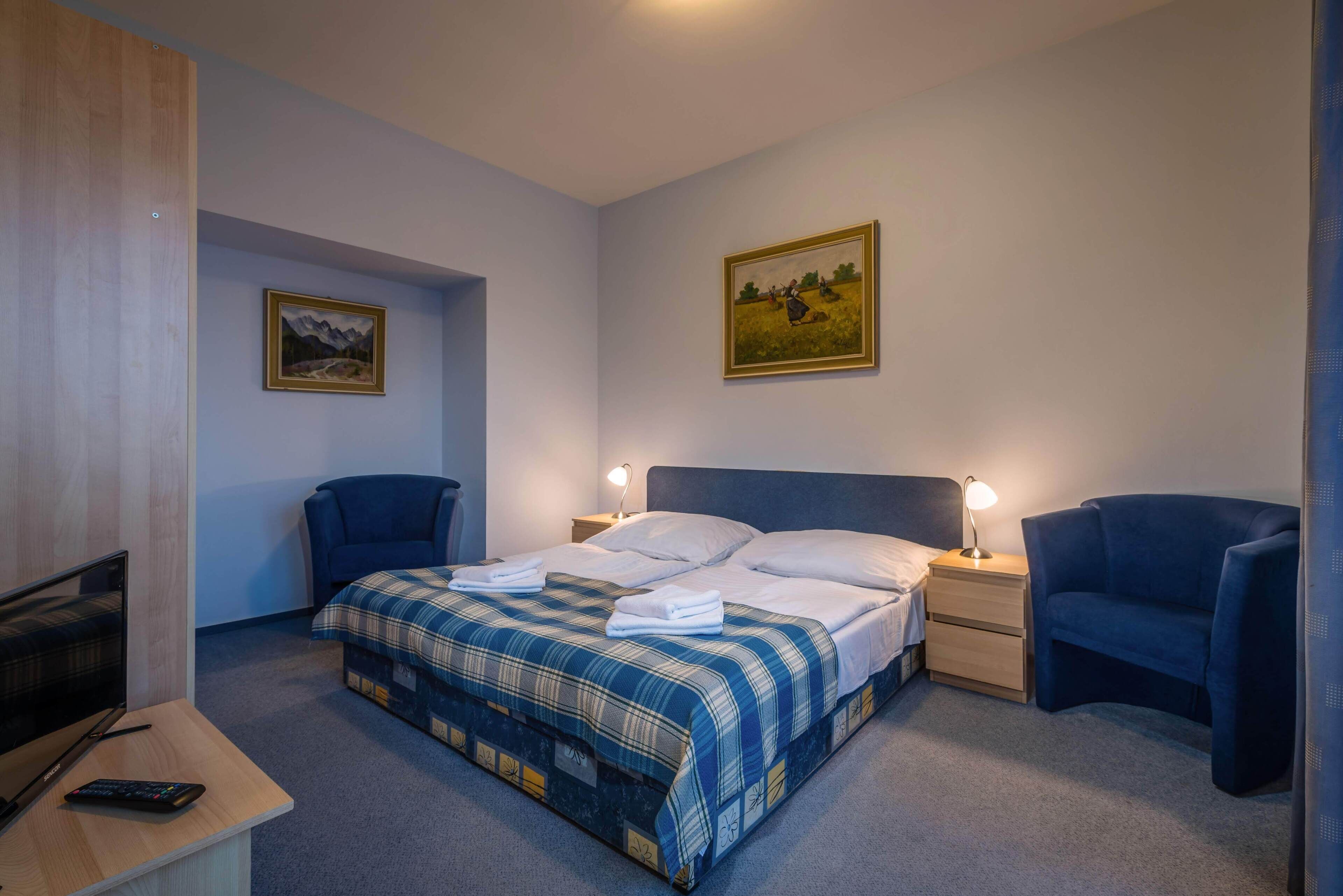 Ein Schlafzimmer mit einem Bett, zwei Nachttischen mit Lampen, einem Schreibtisch mit Fernseher und Fernbedienung sowie zwei Stühlen.