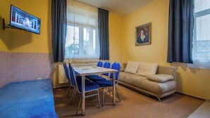 A room with a bed, a dining table with chairs, a sofa, a TV mounted on the wall, and a window with curtains. - Miramonti Apartmany (Vysoké Tatry)