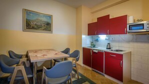 A compact kitchen with red cabinets, a microwave, and a dining area with blue chairs. - Miramonti Apartmany (Vysoké Tatry)