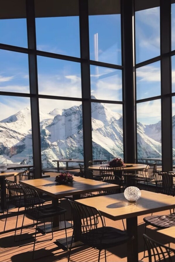 A restaurant with large windows offering a mountain view. Tables are arranged with chairs. - Petit Chalet Pila- Apartment on the slopes (Pila)