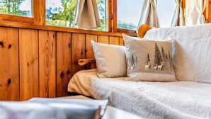 Ein gemütliches Zimmer mit einer Holzwand, einem weißen Sofa mit flauschiger Decke und einem Kissen mit Waldmotiv.