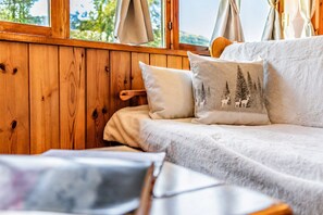 A cozy room with a wooden wall, a white sofa with a fluffy blanket, and a pillow with a forest design. - Petit Chalet Pila- Apartment on the slopes (Pila)