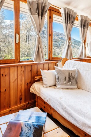 A cozy cabin room with a wooden interior, a sofa with a blanket, and a view of a snowy landscape through the window. - Petit Chalet Pila- Apartment on the slopes (Pila)