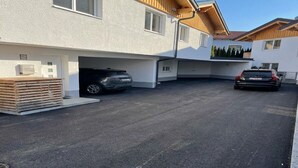 Ein modernes, zweistöckiges Haus mit Garage, einem darin stehenden Auto und einem Stapel Holzbretter davor.