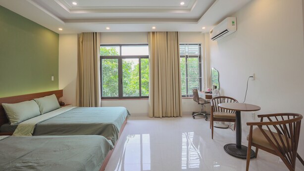 A hotel room with two beds, a desk, a chair, and a window with curtains. - TRÀ HOMESTAY CS3 (Hue)