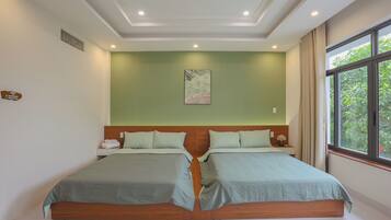 A double bed with a wooden headboard, a bedside table with a lamp, and a window with a view of greenery.