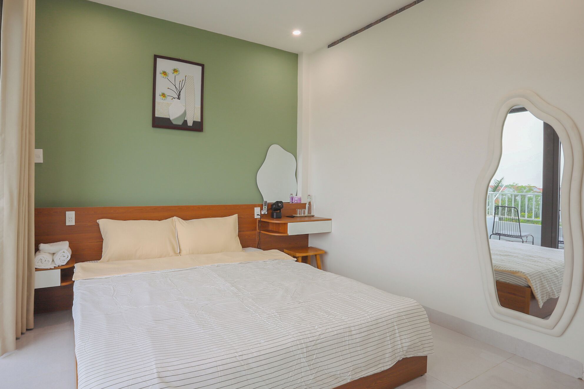 A bedroom with a bed, a bedside table, a mirror, and a window with a view.