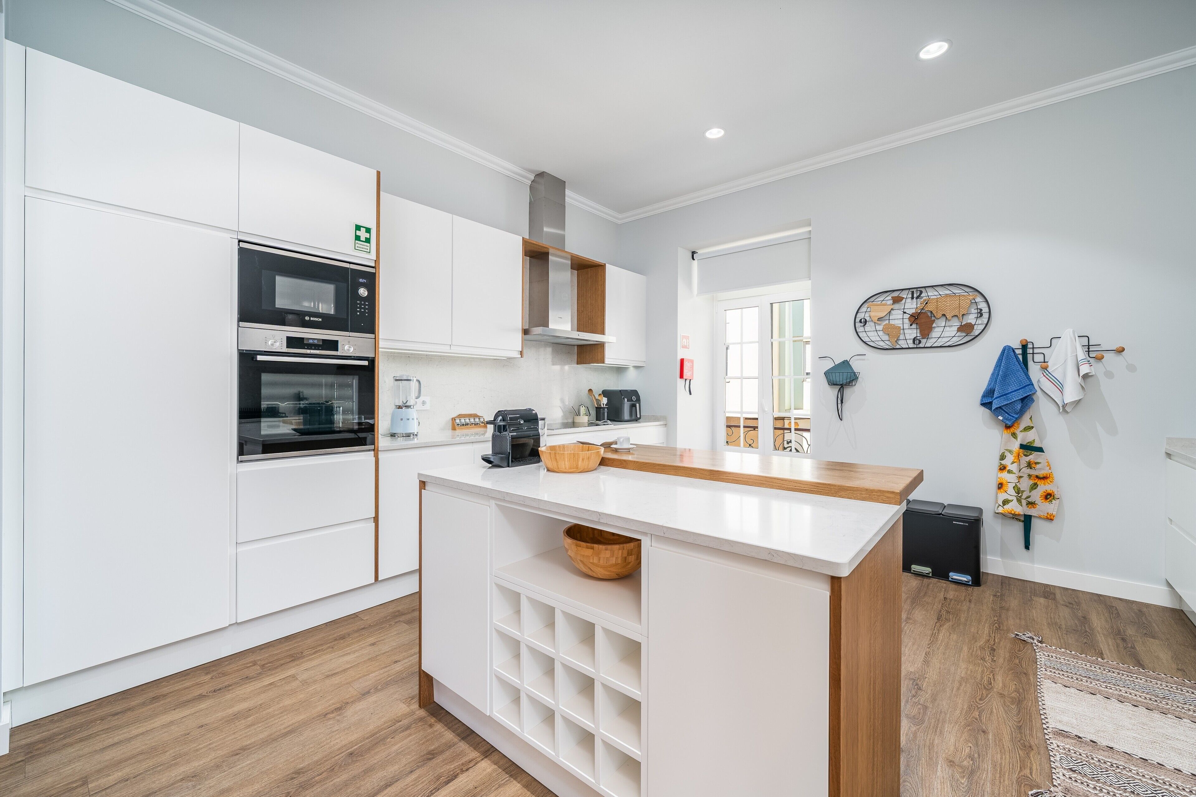 A modern kitchen with white cabinetry, a built-in oven, a coffee machine, and a wooden island with a sink.
