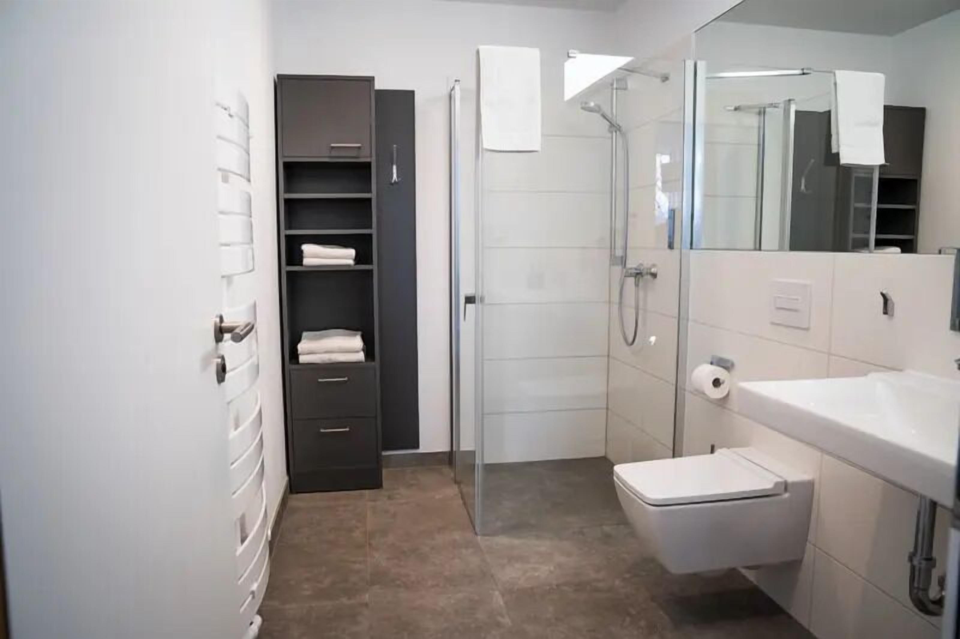 Un baño moderno con ducha, inodoro y un espejo grande.