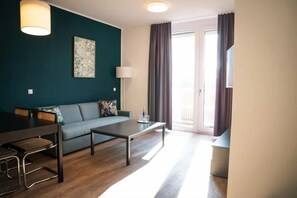 Una sala moderna con un sofá, una mesa de centro y una lámpara. Hay una mesa de comedor con sillas. La habitación tiene un ventanal con cortinas.