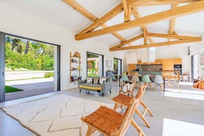 A spacious living area with a large window, wooden beams, a sofa, and a dining area. - Villa des Serpolets, Alpilles view (Maussane-les-Alpilles)