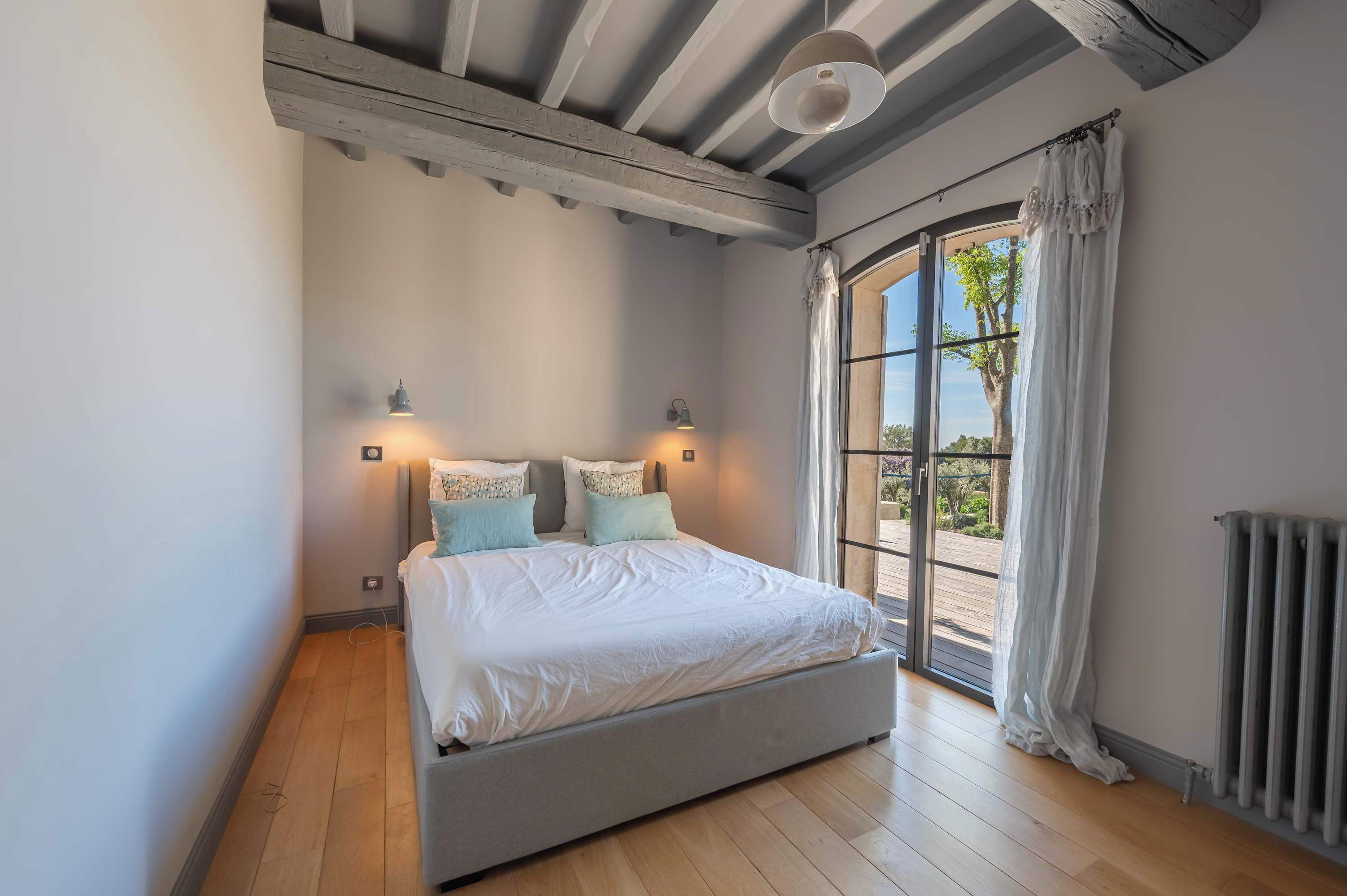 Une chambre à coucher avec un lit, deux lampes fixées au mur, une fenêtre avec des rideaux et un radiateur.