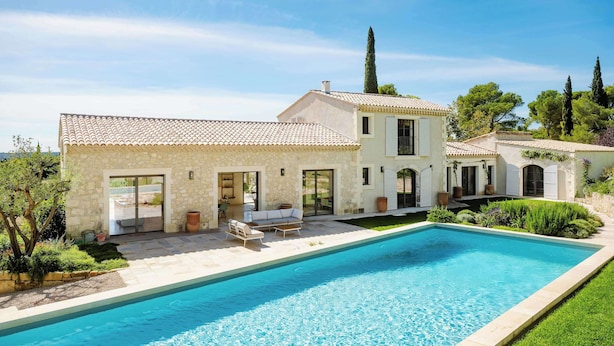Une maison à deux étages avec une piscine, des murs en pierre et un jardin.