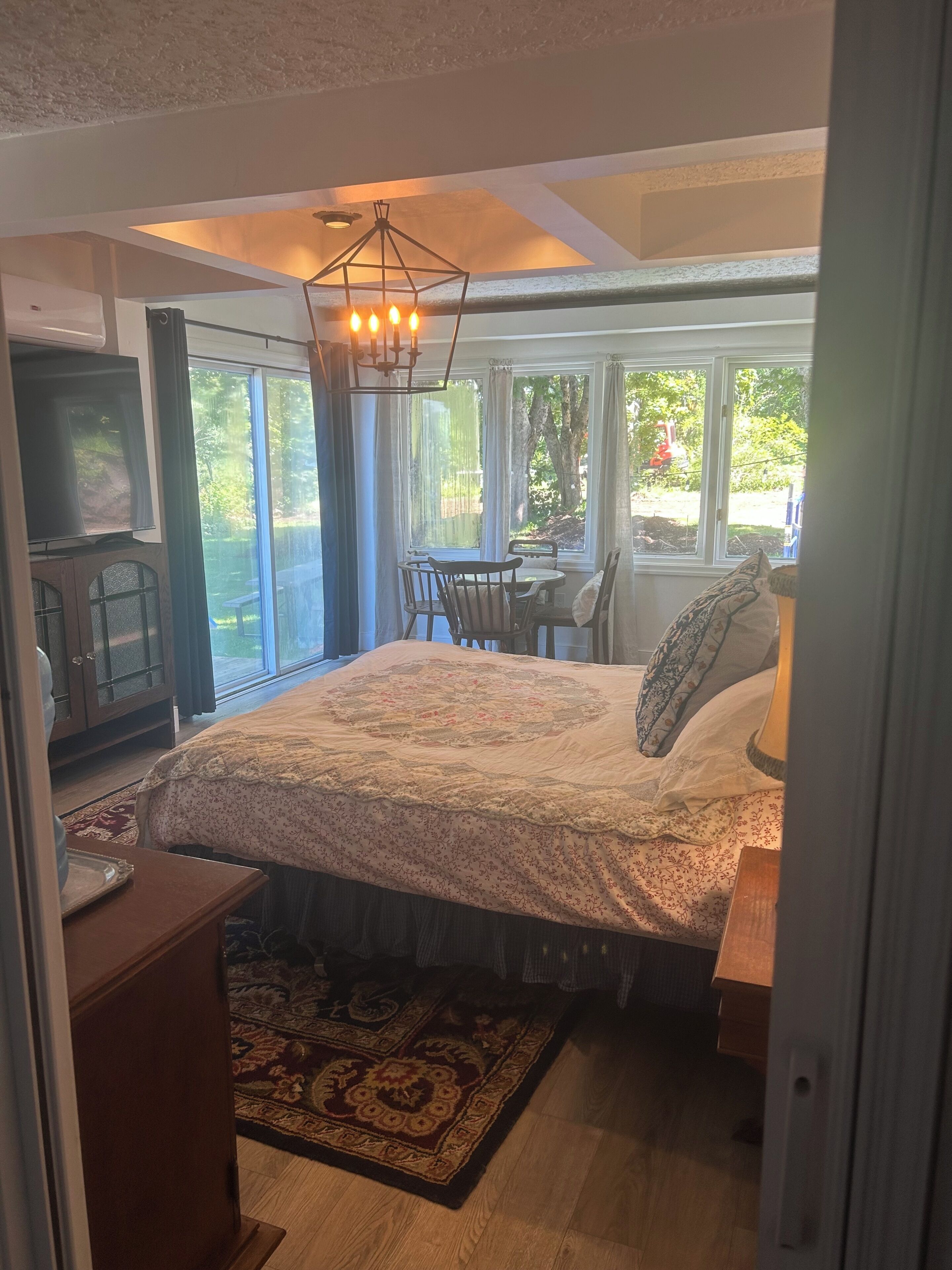 Una camera da letto con un letto grande, una televisione, un'area pranzo con sedie e vista sull'esterno.