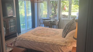 Una camera da letto con un letto grande, una televisione, un'area pranzo con sedie e vista sull'esterno.