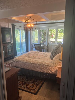 A bedroom with a large bed, a television, a dining area with chairs, and a view of the outdoors.