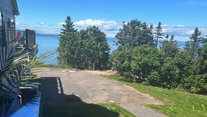 A view of a paved driveway leading to a house with a deck overlooking a body of water and trees.