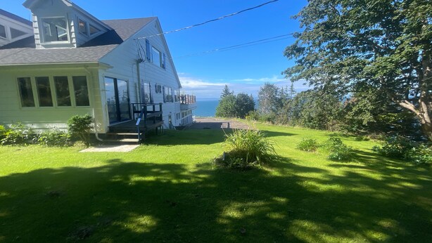 A two-story house with a balcony, a grassy yard, and a view of the ocean.