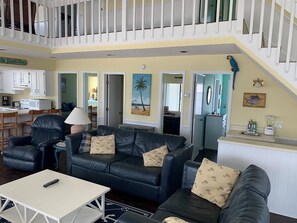 A living room with a black leather sofa, a white coffee table, and a staircase. - Canal Front Home - Sleeps 17! By Williamson Realty (Ocean Isle Beach)