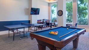 A pool table, ping pong table, dartboard, and a TV in a room with large windows and a carpeted floor. - Charming apartment in beautiful Fort Myers perfect for your getaway (Fort Myers)