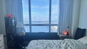 A bedroom with a large window, a bed with floral bedding, a desk with a lamp, and a nightstand with a heater. - Charming apartment in beautiful Fort Myers perfect for your getaway (Fort Myers)