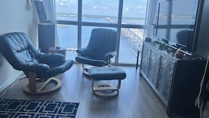 A room with two leather chairs, a wooden cabinet, and a large window offering a view of a body of water and a bridge. - Charming apartment in beautiful Fort Myers perfect for your getaway (Fort Myers)