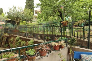 A balcony with potted plants, a metal railing, and a view of a garden and buildings. - Cozy house ideal location for visiting Center Tuscany and on the Francigena (Gambassi Terme)