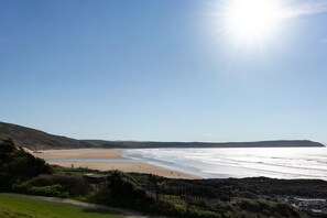 A coastal landscape with a beach, a clear sky, and a sun shining.