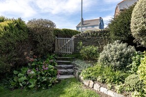 A garden with a stone staircase leading to a wooden gate, surrounded by various plants and a house in the background.