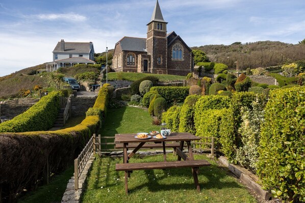 A church with a tower, a stone building, and a well-maintained garden with a picnic table.
