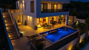 Una casa moderna de dos pisos con piscina, mobiliario exterior y una escalera que lleva al nivel superior.