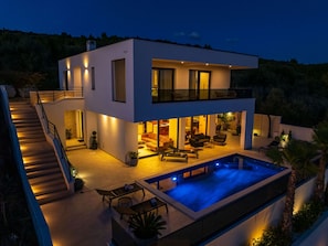 Ein modernes, zweistöckiges Haus mit Swimmingpool, Sitzgelegenheiten im Freien und einer Treppe, die zum oberen Stockwerk führt.