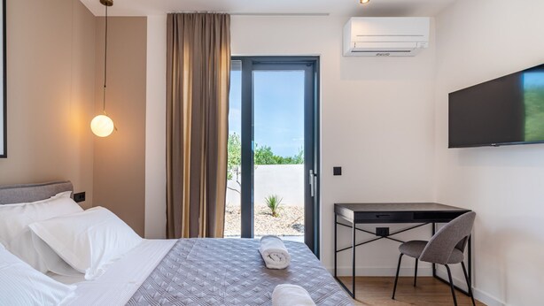 Una habitación de hotel con cama, escritorio, silla, televisor y aire acondicionado.