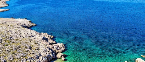 Paesaggio costiero con acque blu cristalline, roccia e spiaggia sabbiosa.