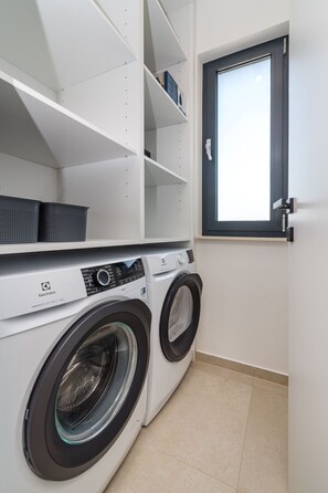 A laundry room with two front-loading washing machines, a window, and white shelving units. - Villa S. by Interhome (Posedarje)