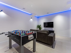 Ein modernes Wohnzimmer mit Tischfußball, einer Couch, einem Fernseher und Einbauleuchten.