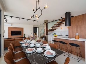 A modern dining area with a long table set for a meal, a kitchen with a wooden staircase, and a living room with a flat-screen TV. - Villa S. by Interhome (Posedarje)