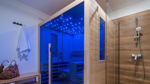 Un baño moderno con ducha envuelta en cristal, paredes de madera y un banco incorporado con toallas.