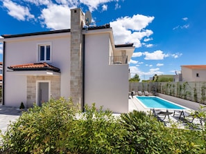 Ein modernes, zweistöckiges Haus mit Swimmingpool, Steinverkleidung und einem Balkon.