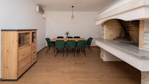 Et spiseområde med et træbord og stole, en hængende lampe og en pejs i sten.