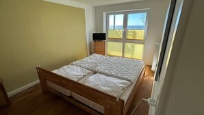 Ein Schlafzimmer mit einem hölzernen Bett, einem kleinen Nachttisch, einem Fernseher auf einem Schrank und einem Fenster mit Jalousien.