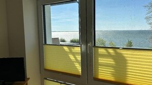 Ein Zimmer mit großem Fenster mit Blick auf ein Gewässer, einem Fernseher auf einem Schrank und einer Tür mit einem gelben Jalousie.