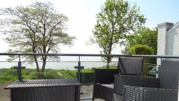 Ein Balkon mit Korbmöbeln, Blick auf Bäume und ein Gebäude im Hintergrund.