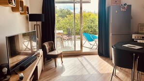 Een moderne woonkamer met een flatscreen televisie, een comfortabele fauteuil, een eettafel en een koelkast.