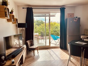 Ein modernes Wohnzimmer mit Flachbildfernseher, einem bequemen Sessel, einem Esstisch und einem Kühlschrank.