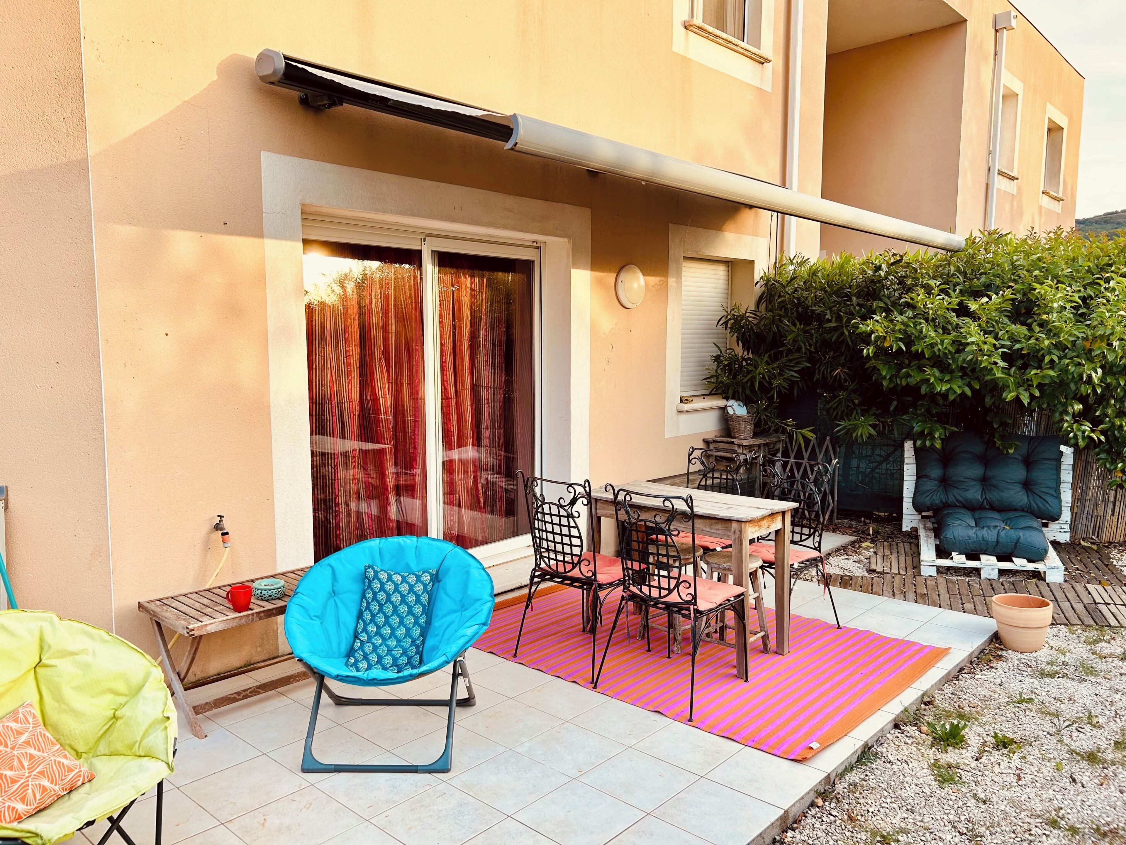 Un patio con tavolo e sedie, una sedia blu, una vaso rosso e una pianta in vaso.