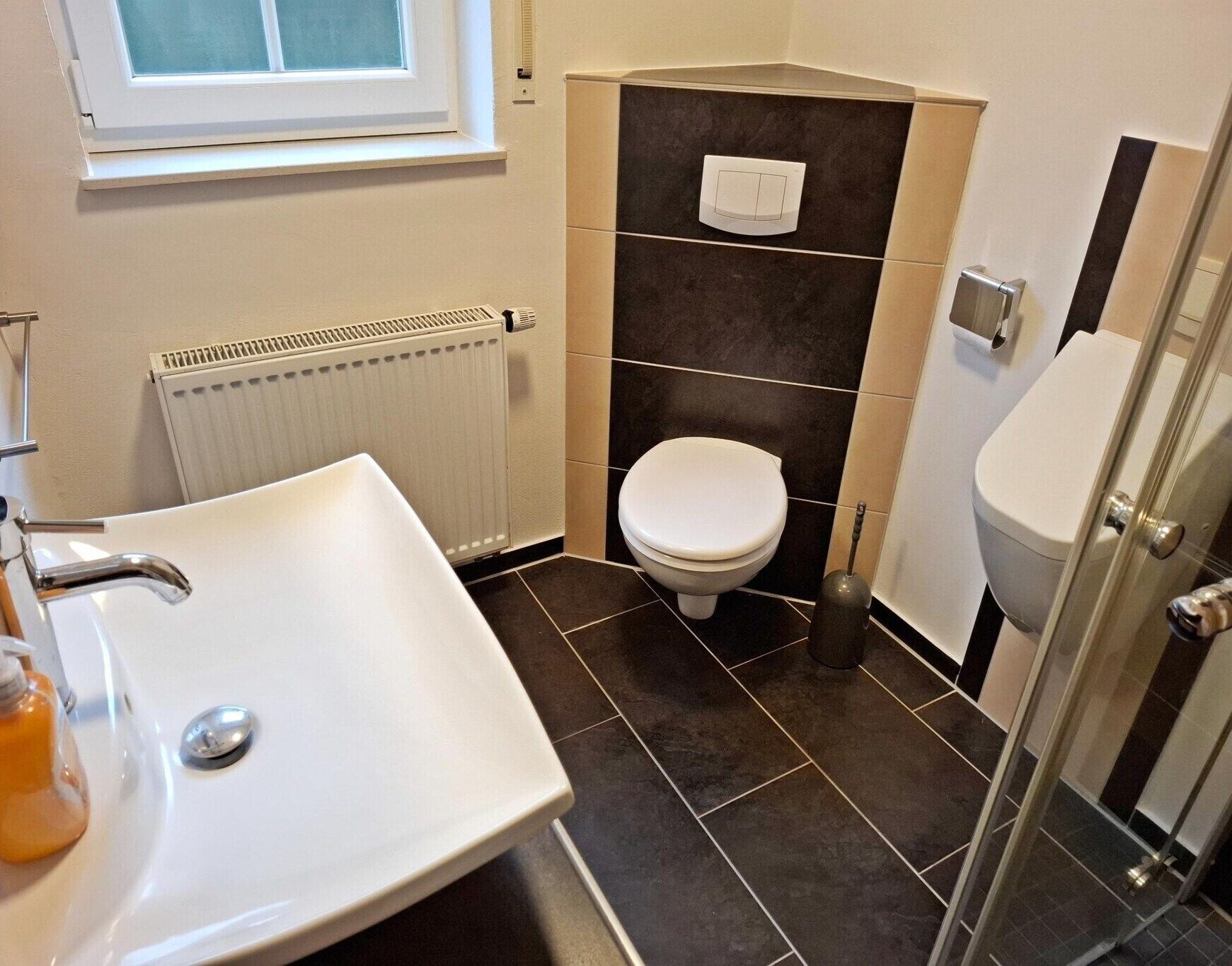 A bathroom with a white sink, a toilet, a radiator, and a glass shower enclosure.